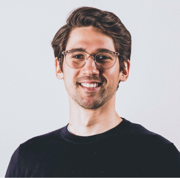 Portrait of a man with brown hair and glasses on a flat gray background.